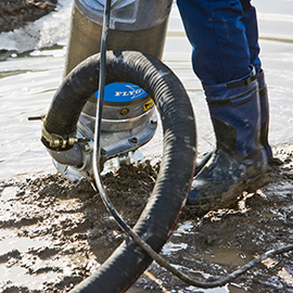 A person in working boots, who is cut off below the knee, is using a Sludge pump in mud